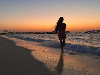 Woman standing on beach against sky during sunset