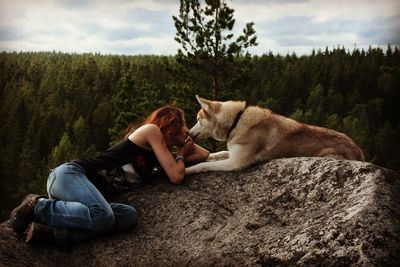 Side view of young woman with siberian husky lying on rock formation