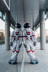 Male astronaut leaning on glass wall while standing on footpath