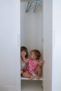 Two little girls looking out of white wardrobe