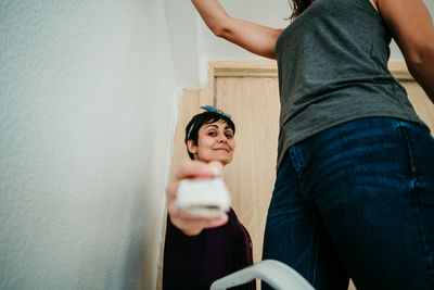 Midsection of woman holding camera while standing against wall at home