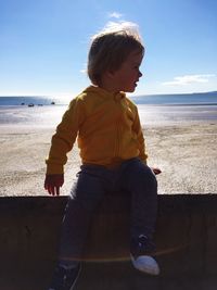 Full length of boy sitting on retaining wall against beach