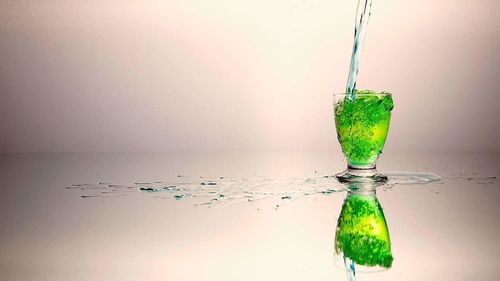 Green water splashing on glass against white background