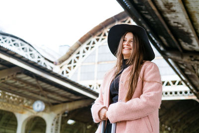 Beautiful young woman in black hat and pink coat with suitcase stands