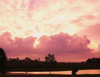 Silhouette trees on landscape against dramatic sky during sunset