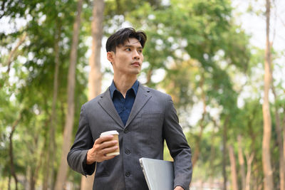 Portrait of young man standing against trees