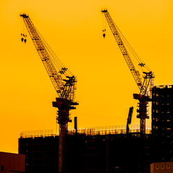 Low angle view of silhouette cranes at construction site against sky during sunset