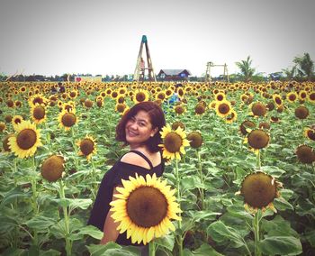 Portrait of smiling young woman with sunflowers on field