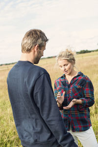 Man and woman talking while standing on grassy field against sky