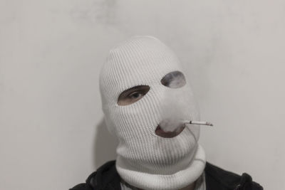 Portrait of person in mask smoking cigarette against wall