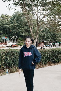 Portrait of smiling young woman standing against trees