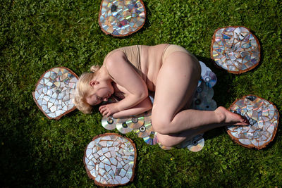 Top view of a young woman lying on a lawn among reflective wooden stumps