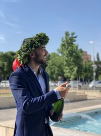 Young woman wearing blazer holding champagne bottle at poolside