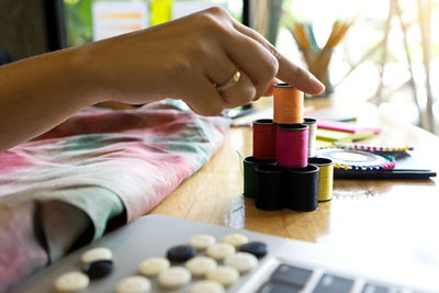 Cropped hand of woman pointing by sewing items at desk