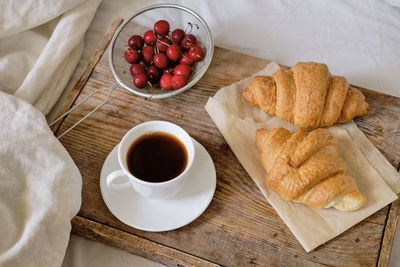 Tasty breakfast with fresh croissant, coffee, cherries on a wooden tray. espresso on a breakfast 