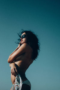 Side view of topless woman standing against clear blue sky