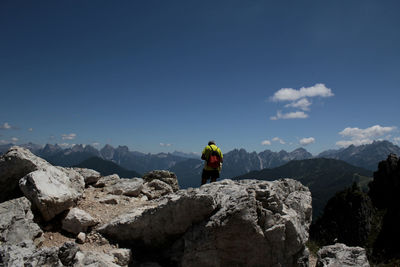 Rear view of man standing on rock against blue sky