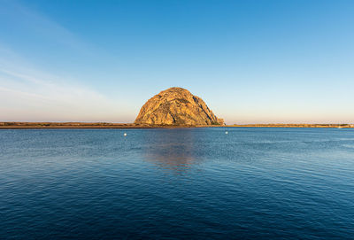 View of rock formation in sea against clear blue sky