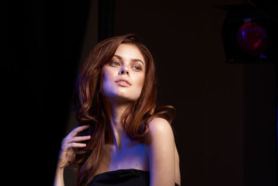 Portrait of young woman looking away against black background