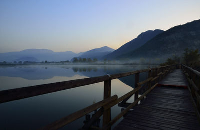 Empty pier over lake against clear sky during sunset