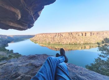 Man sitting on rock by lake against sky