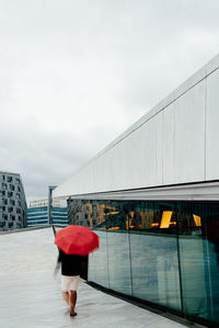 Young adult with red umbrella at modern building. motion blur