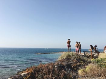 People on calm beach against clear sky