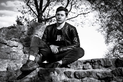 Portrait of young man sitting on rock against trees