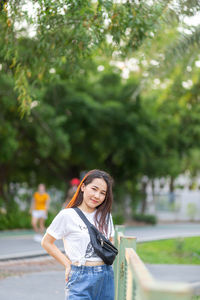 Portrait of smiling young woman standing against trees