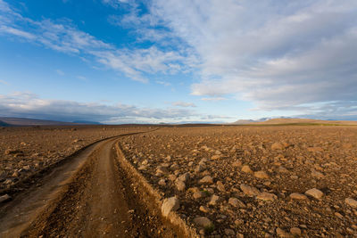 Dirt road by land against sky