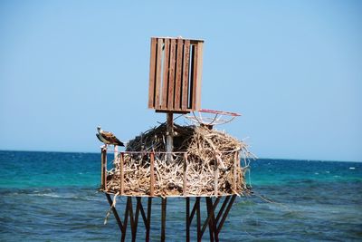 Lifeguard hut on wooden post in sea against clear sky