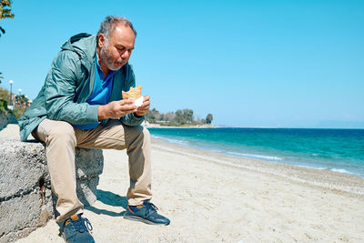 Bearded mature man at spring seaside eating hot palatable panzarotto 