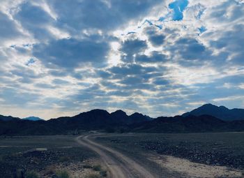 Dirt road amidst landscape against sky