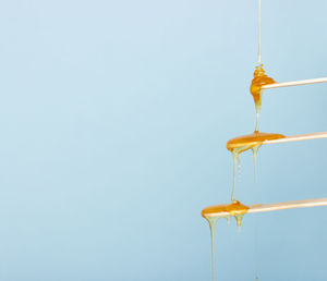 Close-up of yellow drop hanging against blue sky