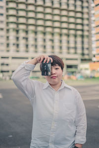Young woman photographing with camera while standing in city