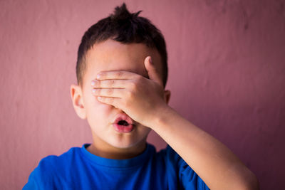 Close-up of boy with hands covering eyes against wall