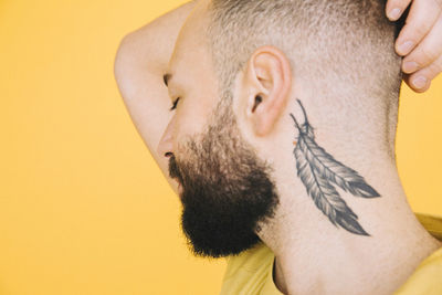 Close-up of neck tattoo on man against yellow background