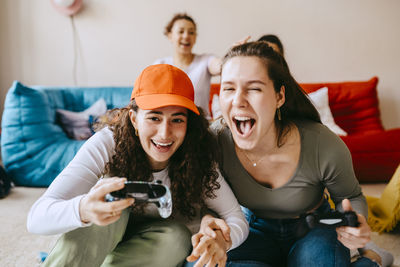 Playful young female friends playing video game at home