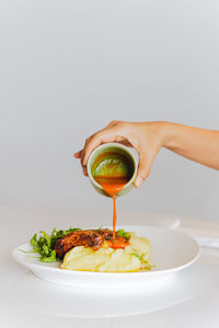 Woman pouring sauce on roasted chicken drumsticks with mash potato on table