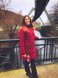 Portrait of smiling young woman standing against railing