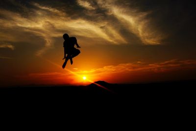 Silhouette man jumping against orange sky