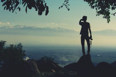 Silhouette man standing on rock by sea against sky