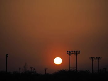 Silhouette street lights against orange sky during sunset