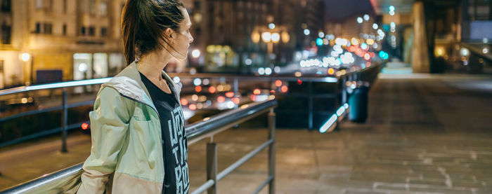 Woman wearing sportswear looking to empty sidewalk at night in town