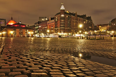 Illuminated buildings by street against sky at night