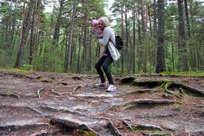 Full length of woman carrying daughter while standing in forest