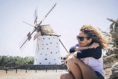 Young woman sitting on traditional windmill against sky