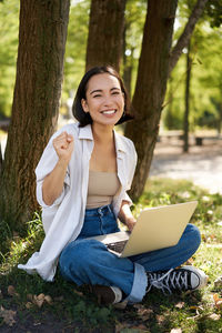 Portrait of young woman using laptop while sitting in forest