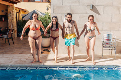 Full length friends holding hands while standing at poolside