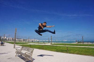 Full length of man jumping at park against blue sky